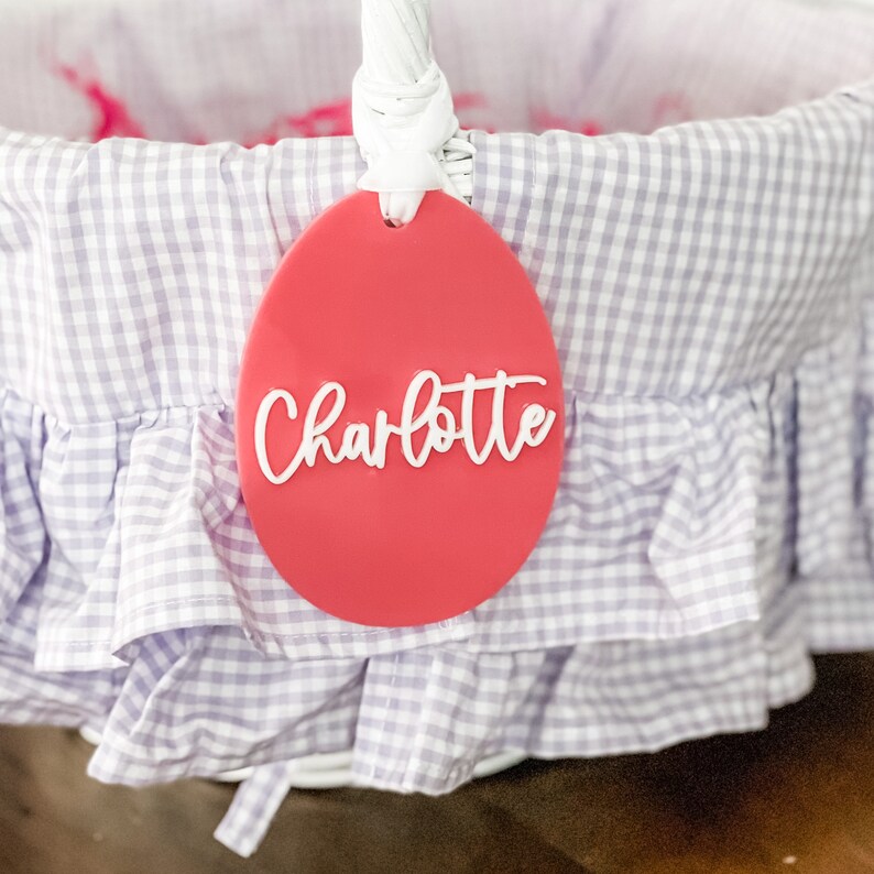May include: A pink Easter basket tag with the name Charlotte written in white cursive lettering.