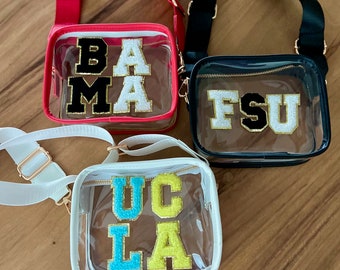 May include: Three clear plastic bags with adjustable straps. The bags are decorated with colorful felt letters spelling out "BAMA", "FSU", and "UCLA".
