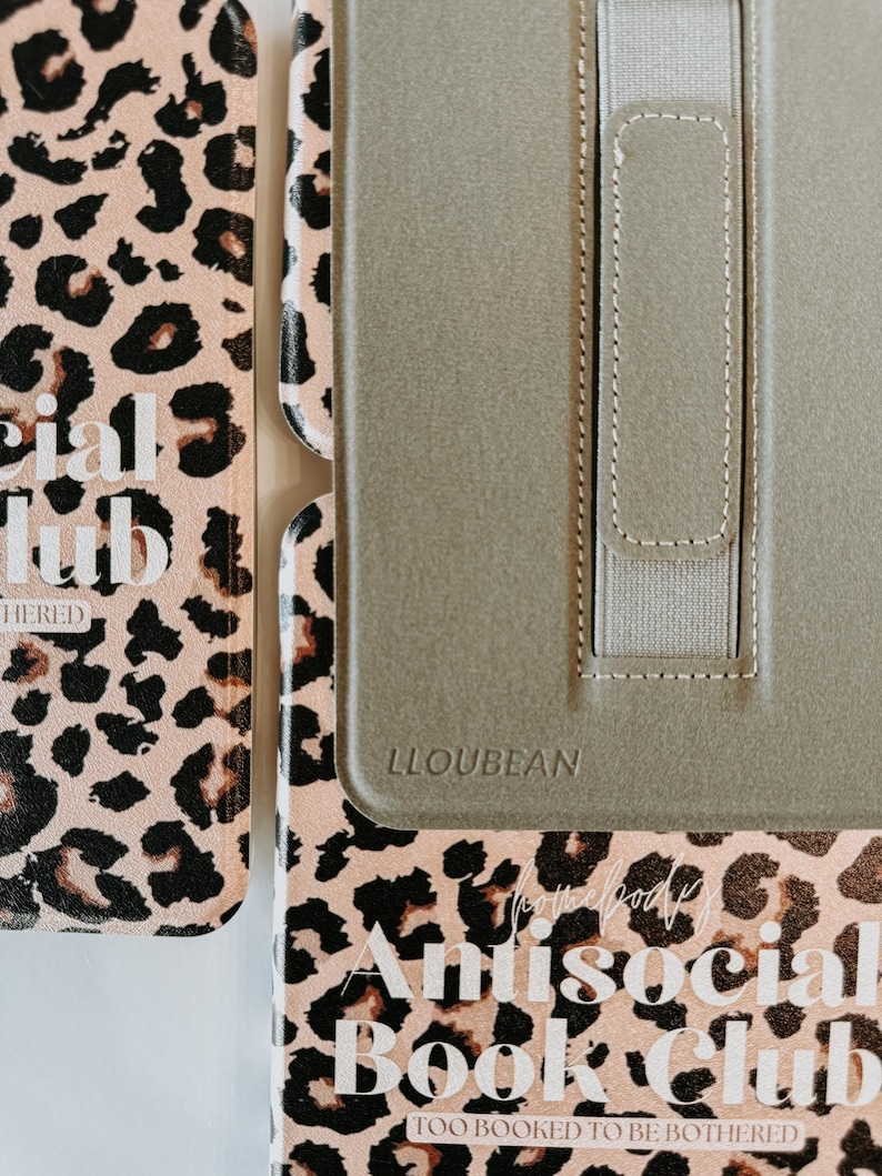 May include: A close-up of a book cover and a tablet case. The book cover has a pink leopard print with the words "Antisocial Book Club" and "Too Booked to be Bothered". The tablet case is olive green with the brand name "LLOUBEAN".
