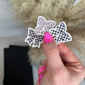 Può includere: Tre adesivi a forma di fiocco, uno con un motivo a scacchi in bianco e nero e due con un motivo a scacchi in marrone e bianco.