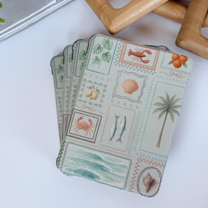 May include: A stack of four square coasters with a light green background and a repeating pattern of framed sea-themed illustrations. The illustrations include a lobster, seashell, crab, fish, and palm tree. The coasters are made of a durable material.