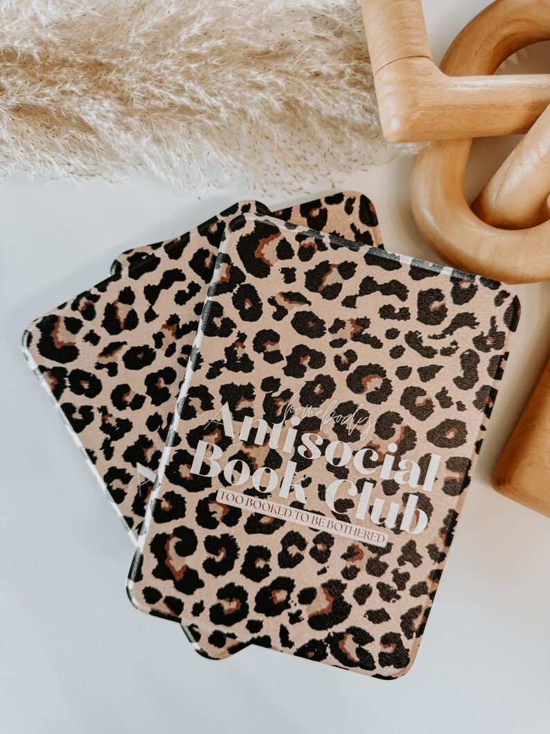 May include: Two leopard print book covers with the text "Antisocial Book Club: Too Booked To Be Bothered". The covers are tan with black and brown spots.