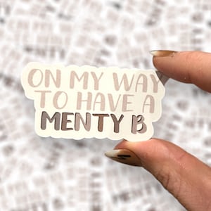 May include: A white sticker with the text "On my way to have a menty b" in brown and white lettering.