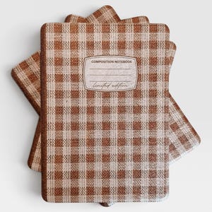 May include: A stack of three rectangular composition notebooks featuring a brown and white gingham check pattern. Each notebook has a central white label with the printed text COMPOSITION NOTEBOOK and the cursive script Limited edition.