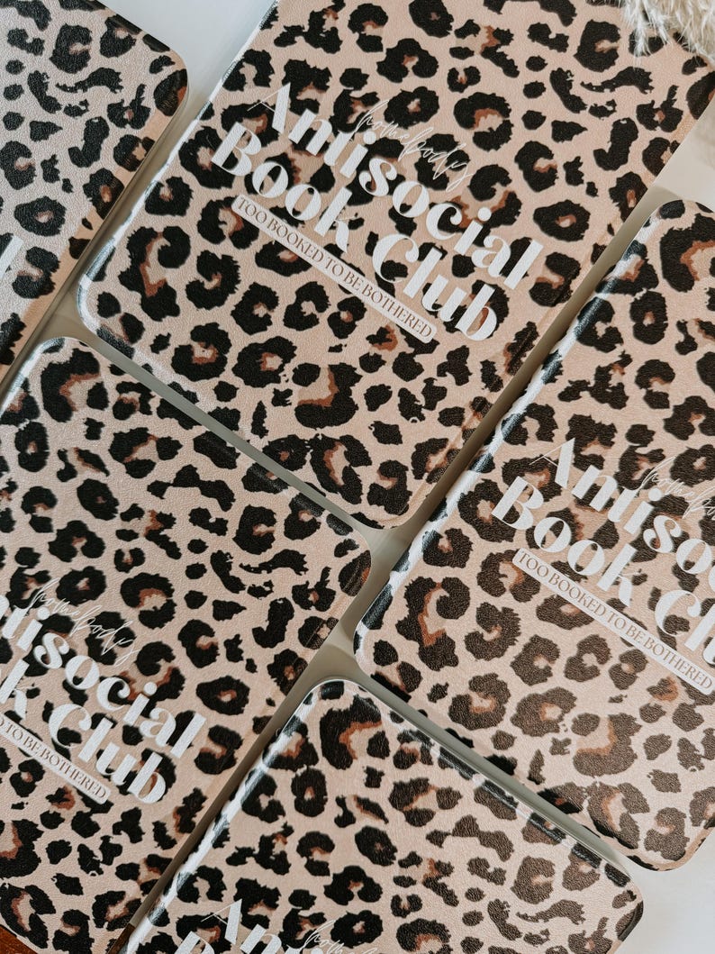 May include: Several rectangular book covers with a tan leopard print pattern. The covers have the text "Antisocial Book Club" and "Too Booked to be Bothered" in white lettering. The covers are arranged in a close-up shot.