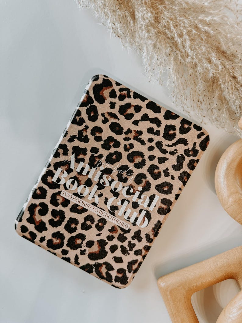 May include: A rectangular book cover with a leopard print pattern in shades of brown and black. The cover features the text "Antisocial Book Club" in white, with "Too Booked to be Bothered" below. The background is white.