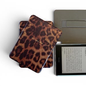 May include: An e-reader device featuring a protective cover with a brown and black leopard print pattern and the text "HOT GIRLS READ" in gold lettering. The device is shown with its screen active, displaying text from a book page.