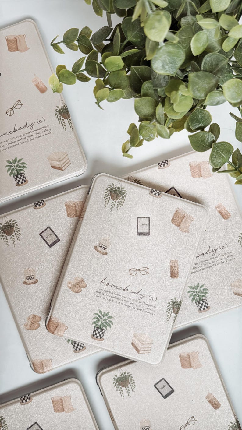 May include: Beige Kindle covers with a repeating pattern of potted plants, books, eyeglasses, and coffee cups. The word "homebody" is printed on the cover. Green leaves are in the background.