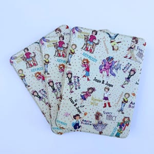 May include: A set of three cream-colored cardholders featuring illustrations of children and book titles like "Judy Moody," "Junie B. Jones," and "Amelia Bedelia." The cardholders have a repeating pattern of characters.