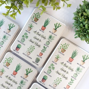 May include: Several rectangular coasters with a botanical theme are displayed. Each coaster features illustrations of various houseplants, labeled with their common names. The text "A Book Girls Guide to House Plants" is also present on each coaster.