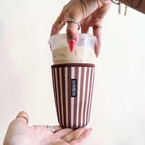 May include: A brown and white vertically striped fabric cup sleeve featuring a black rectangular label with the white text LOUBEAN printed vertically. The sleeve is designed to fit around a clear plastic cup filled with a light beige iced beverage.
