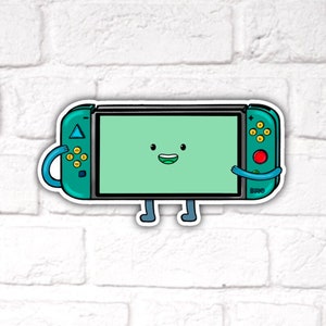 May include: A teal green Nintendo Switch console with a smiling face and cartoon arms and legs. The console has a green screen and yellow buttons.