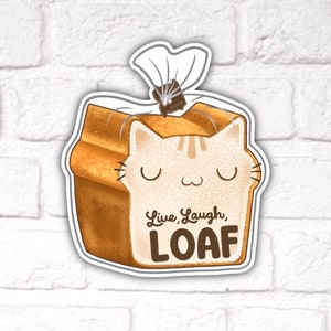 May include: A cartoon cat loaf of bread with a plastic bag on top. The bread has a brown crust and a white interior. The cat has closed eyes and a light brown and white striped pattern. The text on the bread reads "Live, Laugh, LOAF".
