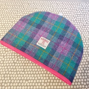 Puede incluir: Un calienta-té de cuadros en azul verdoso, rosa y amarillo con ribete rosa. El calienta-té tiene una etiqueta que dice "Harris Tweed".