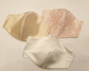 Puede incluir: Tres mascarillas faciales de tejido satinado. Una mascarilla es de color marfil con un delicado bordado de encaje rosa. Las otras dos mascarillas son de satén marfil liso.
