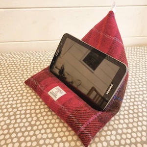 Könnte beinhalten: Ein roter und blauer karierter Tablet-Ständer aus Stoff. Der Ständer hat die Form einer Pyramide und ist so konzipiert, dass er ein Tablet aufrecht hält. Ein schwarzes Tablet mit dem Samsung-Logo liegt im Ständer.