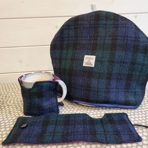 Könnte beinhalten: Ein Set aus drei Teekosys in den Farben Teal, Schwarz und Marineblau mit Karomuster. Das Set beinhaltet einen Teekosys für die Teekanne, einen Teekosys für die Tasse und einen Teekosys für eine Teetasse. Die Teekosys sind aus einem weichen, gewebten Stoff mit violettem Besatz gefertigt.
