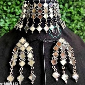 Op de afbeelding: Een zilveren choker ketting en oorbellen set met hangende gespiegelde vierkanten. De ketting is een brede band met meerdere rijen gespiegelde vierkanten. De oorbellen zijn lang en hebben drie rijen gespiegelde vierkanten.