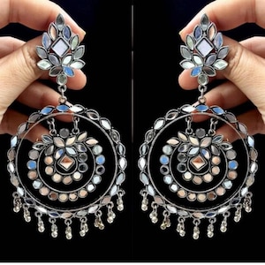 Puede incluir: Un par de pendientes de plata con varios espejos redondos y un borla colgante. Los pendientes tienen un diseño floral en la parte superior.