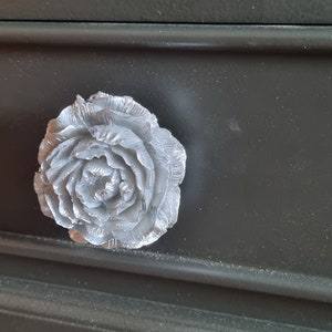 May include: A silver-coloured rose-shaped drawer pull on a black dresser.