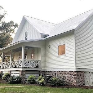 May include: A two-story white house with a metal roof and a porch. The house has a brick foundation and a green lawn. The porch has a white railing and a covered area. The house has several windows and a door.