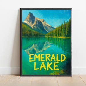 May include: A framed art print featuring a scenic landscape of Emerald Lake. The artwork depicts a mountain range reflected in the lake's turquoise waters, with evergreen trees lining the shores. The words "EMERALD LAKE" are written in yellow.