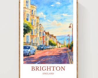 May include: Watercolor print of Brighton, England, featuring a street scene with colorful buildings, parked cars, and a church steeple in the distance. The sky is blue with fluffy clouds. The print is framed in a wooden frame.