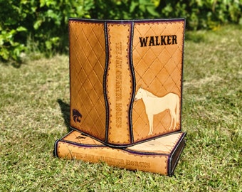 Puede incluir: Dos diarios encuadernados en cuero marrón con un patrón acolchado. El diario superior tiene una silueta de caballo y el texto "WALKER" en la portada. El diario inferior tiene el texto "TEE JAY QUARTER HORSES" en la portada.