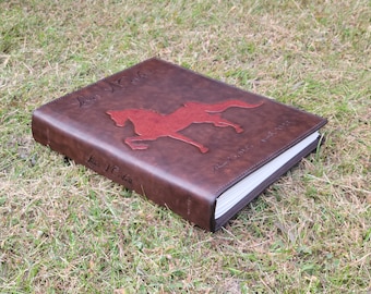 Puede incluir: Un álbum de fotos encuadernado en cuero marrón con una silueta de caballo roja en relieve en la portada. El álbum se titula "Love & Horses" y tiene el nombre "Lisa J.C. Gill" en relieve en el lomo.