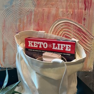 May include: A white canvas tote bag with a red book titled "Keto Life" inside. The book has the text "Over 100 Healthy and Delicious Ketogenic Recipes".