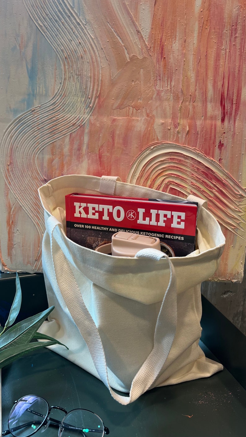 May include: A white canvas tote bag with a red book titled "Keto Life" inside. The book has the text "Over 100 Healthy and Delicious Ketogenic Recipes".