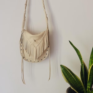 Bolso estilo western de piel de ciervo color crema con flecos y tachuelas metálicas.