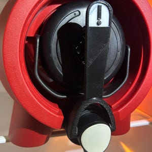 May include: A red circular beverage dispenser frame with a black internal component. A black lever with a white exclamation point icon is attached to the front. The dispenser features a black spout with a white circular end piece for liquid flow.