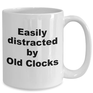 May include: White ceramic coffee mug with black text that reads "Easily distracted by Old Clocks".