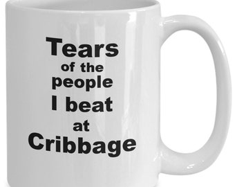May include: White ceramic mug with a curved handle. The mug features the text "Tears of the people I beat at Cribbage" in black, bold font. The mug is designed for hot beverages.