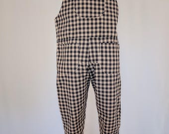 May include: Overalls in a black and tan checkered pattern. The overalls have adjustable straps, a front pocket, and two back pockets. The garment is displayed on a mannequin.