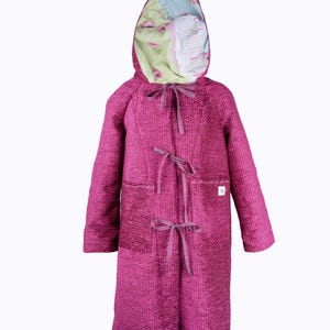 May include: A long, magenta coat with a hood. The coat has a textured weave and is fastened with ribbon ties. The hood's interior is lined with floral patterned fabric in shades of green, pink, and blue. The coat has two pockets.