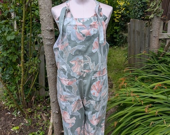 May include: Green floral overalls with a tie at the neck. The overalls have a large pocket on the front and a small pocket on the back. The fabric is a light weight cotton.