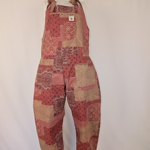 Può includere: Tuta patchwork nei toni del rosso e beige, con motivi a righe e paisley. La tuta ha un top a pettorina con spalline annodabili e tasche. Il tessuto è un materiale morbido e tessuto, ideale per l'abbigliamento casual.