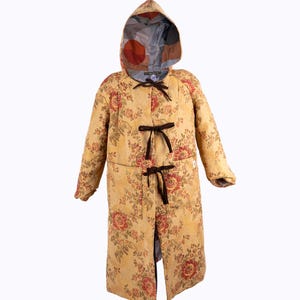 May include: A long, hooded coat with a floral pattern in yellow, red, and green. The coat features dark brown ties and a patterned hood lining. The coat is designed with a relaxed fit and is suitable for various occasions.
