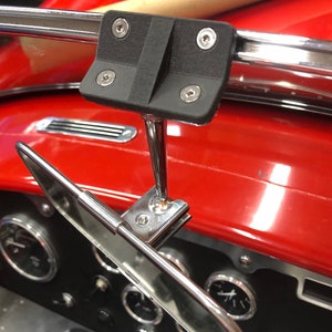 May include: A black rearview mirror mount with a silver metal arm and a black mirror. The mount is attached to a red car dashboard with a chrome trim.