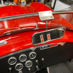 Puede incluir: Tablero rojo de un coche clásico con un espejo retrovisor cromado, indicadores y un salpicadero negro. Los limpiaparabrisas son visibles y la carrocería del coche es de color rojo brillante.