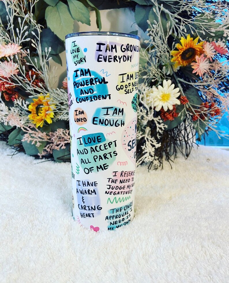 May include: White stainless steel tumbler with a lid, featuring handwritten affirmations and colorful abstract shapes. Text includes phrases like "I am powerful and confident" and "I am enough". A motivational and inspirational item.