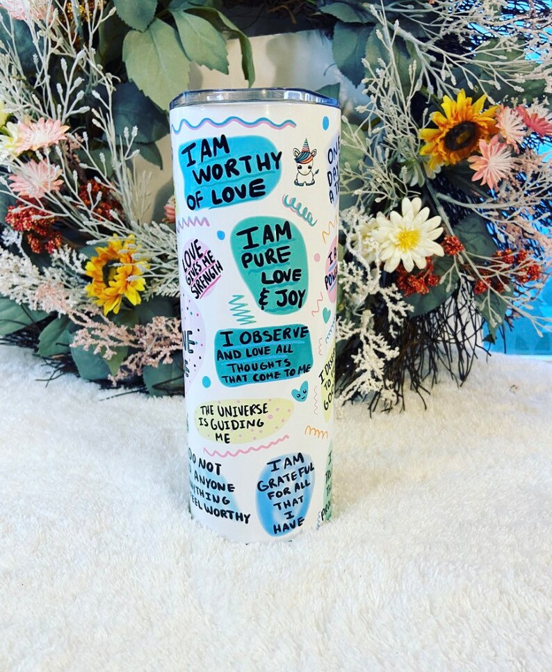 May include: A white stainless steel tumbler with a colorful design featuring affirmations like "I am worthy of love" and "I am pure love & joy." The tumbler has a unicorn graphic and various text bubbles with positive messages.