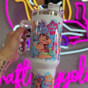 Puede incluir: Vaso blanco con asa y tapa, decorado con personajes de dibujos animados y motivos florales. El dise&ntilde;o presenta a Lilo y Stitch, con un tema tropical. El vaso est&aacute; dise&ntilde;ado para contener aproximadamente 887 ml.