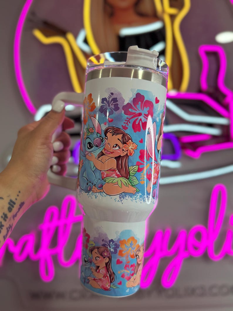 Puede incluir: Vaso blanco con asa y tapa, decorado con personajes de dibujos animados y motivos florales. El dise&ntilde;o presenta a Lilo y Stitch, con un tema tropical. El vaso est&aacute; dise&ntilde;ado para contener aproximadamente 887 ml.