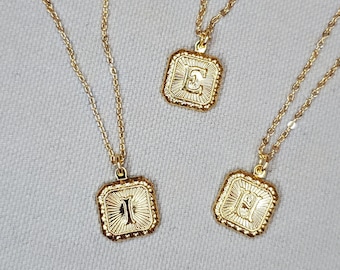 Könnte beinhalten: Drei goldene Halsketten mit quadratischen Anhängern, die die Buchstaben E, I und H zeigen. Die Anhänger haben ein strukturiertes, verziertes Design.