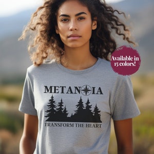May include: A heather gray t-shirt with the word "METANOIA" above a silhouette of pine trees and the phrase "TRANSFORM THE HEART." A circular graphic states "Available in 15 colors!"