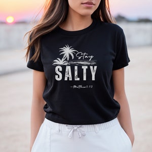 K&ouml;nnte beinhalten: Ein schwarzes T-Shirt mit einer wei&szlig;en Grafik von Palmen und dem Text "Stay Salty - Matthew 5:13".