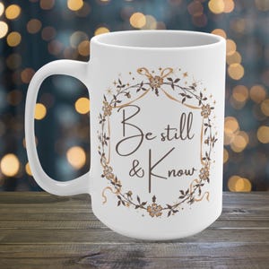 May include: White ceramic mug with a brown floral design and the text "Be still & Know" in brown lettering.